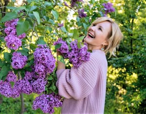 A smiling woman in a garden surrounded by purple flowers