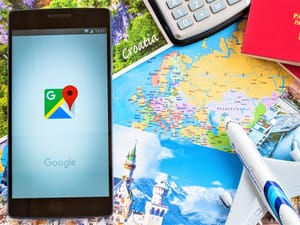 A phone with Google Maps app opened on top of postcards, a map, a passport and a calculator
