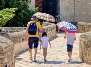 Father protects his children with umbrellas from the sun on a very hot day.