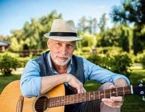 An old man wearing a hat and holding a guitar outside