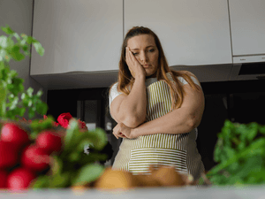 exhausted woman thinking about healthy meal options, with a lot of vegetables in front of her on a kitchen counter