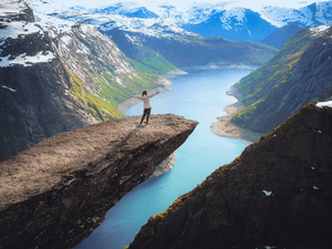 Young woman standing on the edge of a cliff, above the lake surrounded by mountains, Norway.