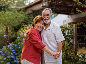 An old married couple hugging each other in their garden