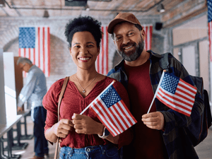 portrait of a couple holding American flags in their hands, after casting their vote