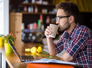 A guy drinking coffee and looking at his laptop.