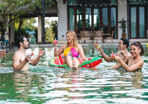 A group of friends drinking cocktails and having a good time in a pool.