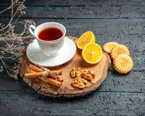 A cup of tea served with lemon, biscuits, walnuts and cinnamon sticks.