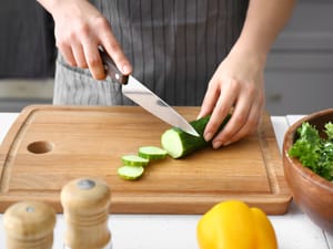 Person cutting cucumber on chopping board.