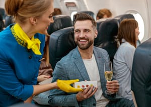 A man on a plane holding a glass of wine and talking to the flight attendant.