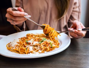 A close-up of a woman eating spaghetti with a spoon and a fork