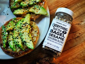 Jar of Trader Joe's "Everything but the Bagel" seasoning blend next to a plate with a bagel with avocado.