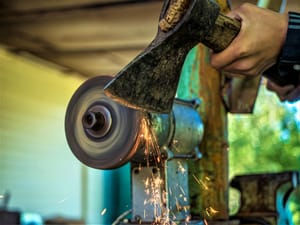 A person sharpening an ax using an electric grinder