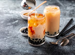 Two glasses of Thai bubble tea, with milk being poured into one of them.