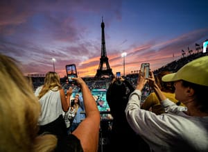Spectators photograph a colorful sunset at Eiffel Tower Stadium prior to a beach volleyball match between The United States and Canada at the 2024 Summer Olympics, Saturday, July 27, 2024, in Paris, France.