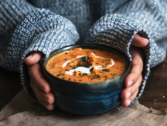 Female hands holding a bowl of pumpkin soup and wearing a sweater. 