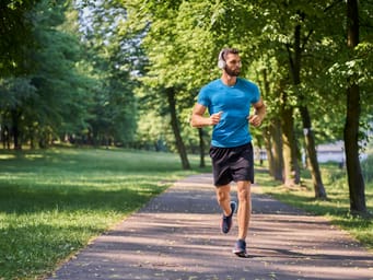 A young man running in the park with headphones on a sunny summer day.
