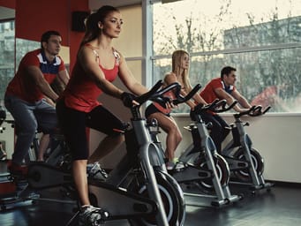 A group of young, active people exercising in a spinning class, intensely focused on their workout in the gym.