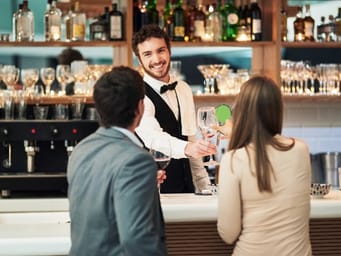 A barman serving a couple alcohol drinks at a hotel bar, creating a hospitable and happy atmosphere.