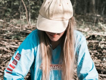A woman in a blue jacket and white cap sitting on the ground.