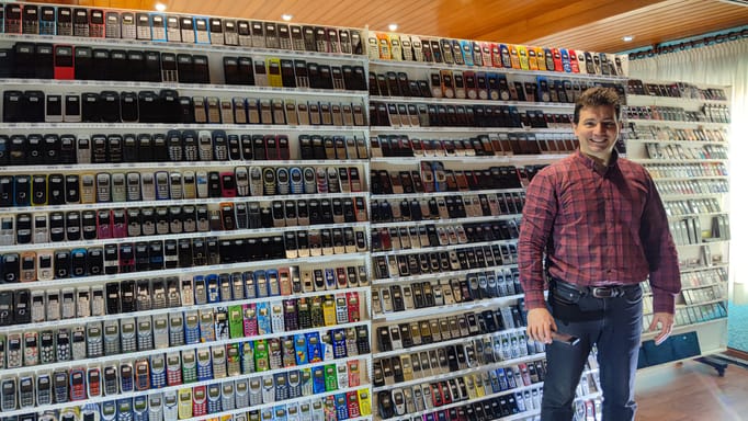Wences Palau Fernandez smiling in a room filled with shelves of old Nokia mobile phones.